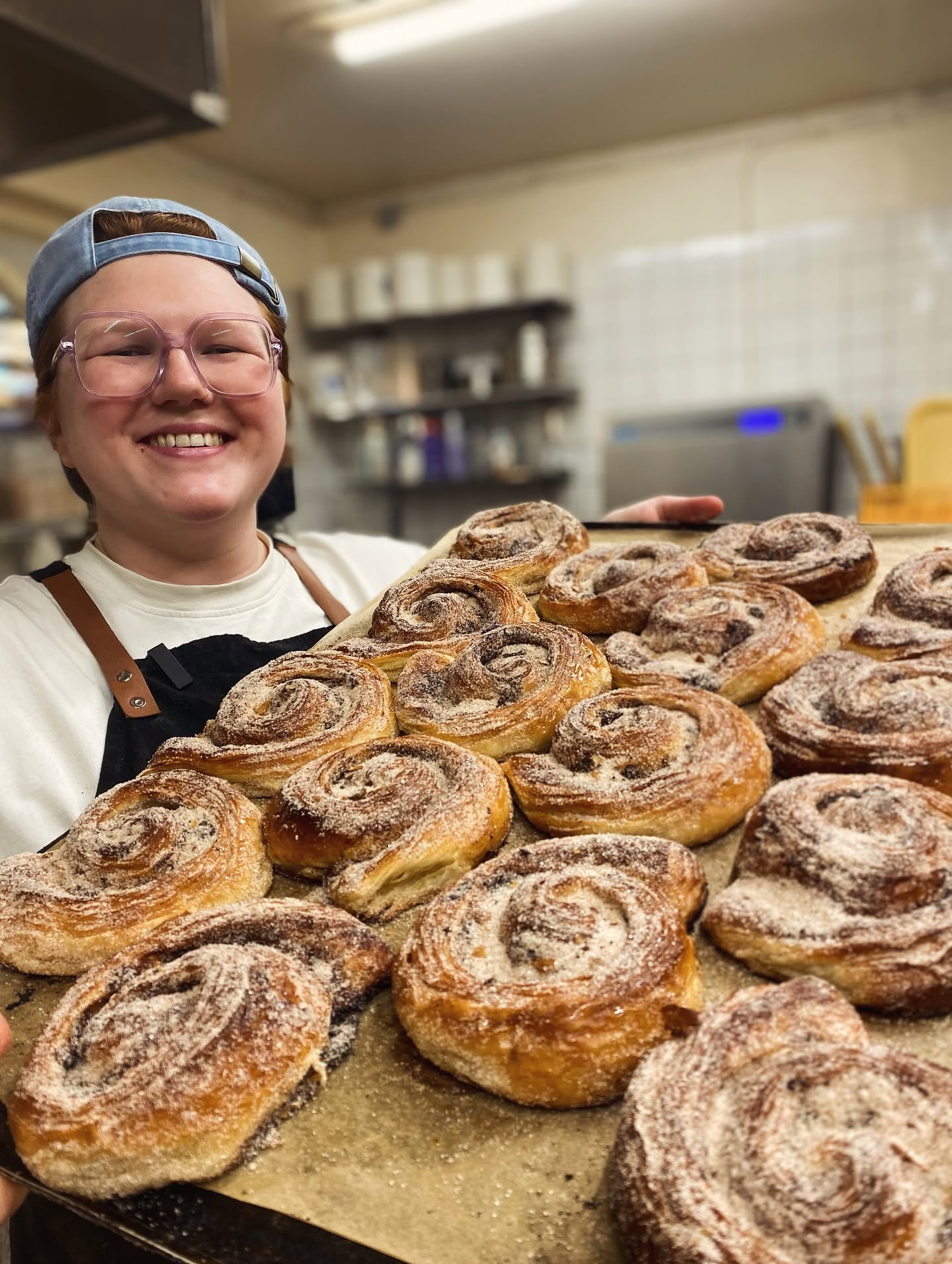 Plåt med nybakade kanelbullar hålls upp i bageriet